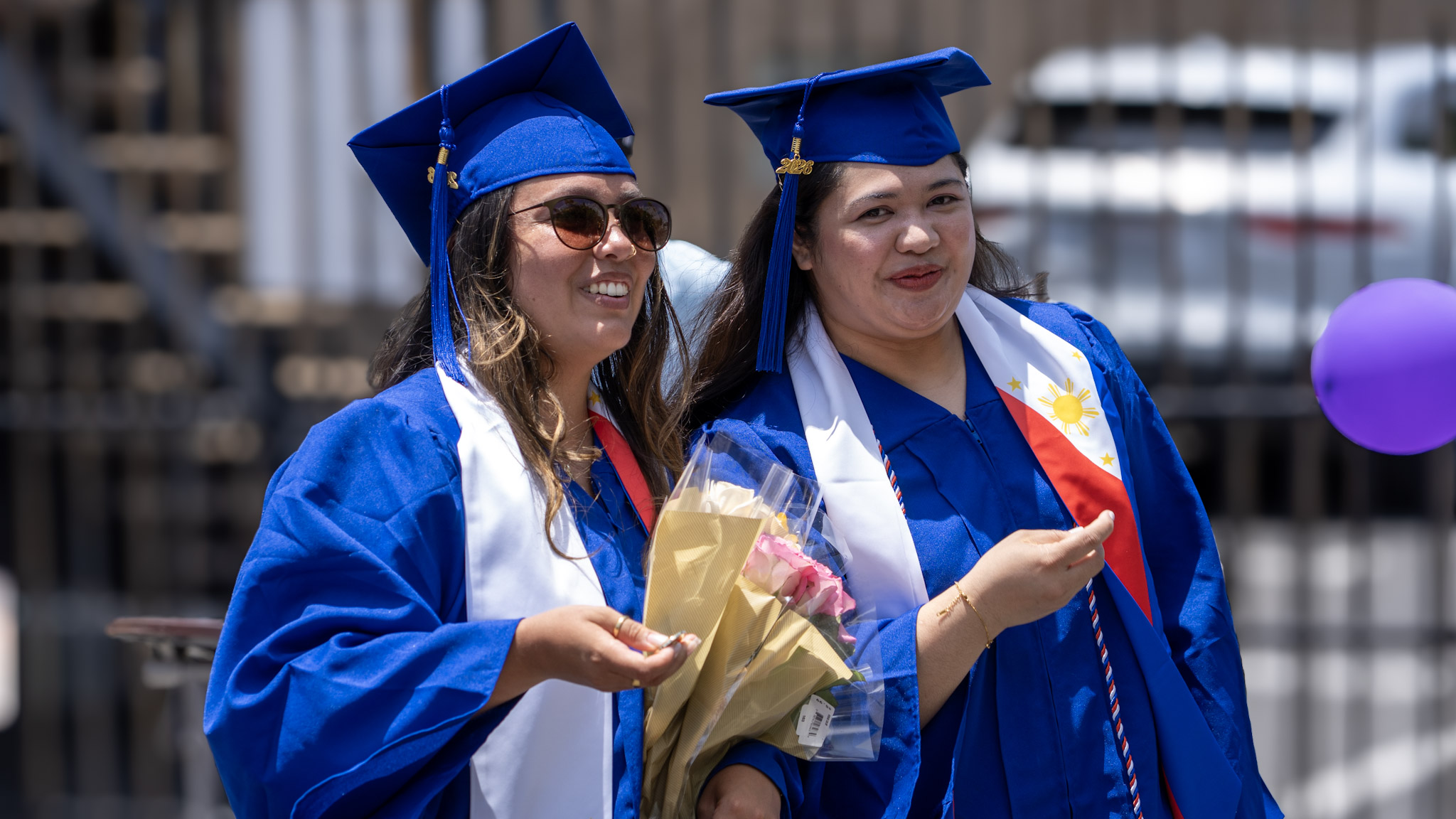 Two graduates celebrating outside with flowers and diploma