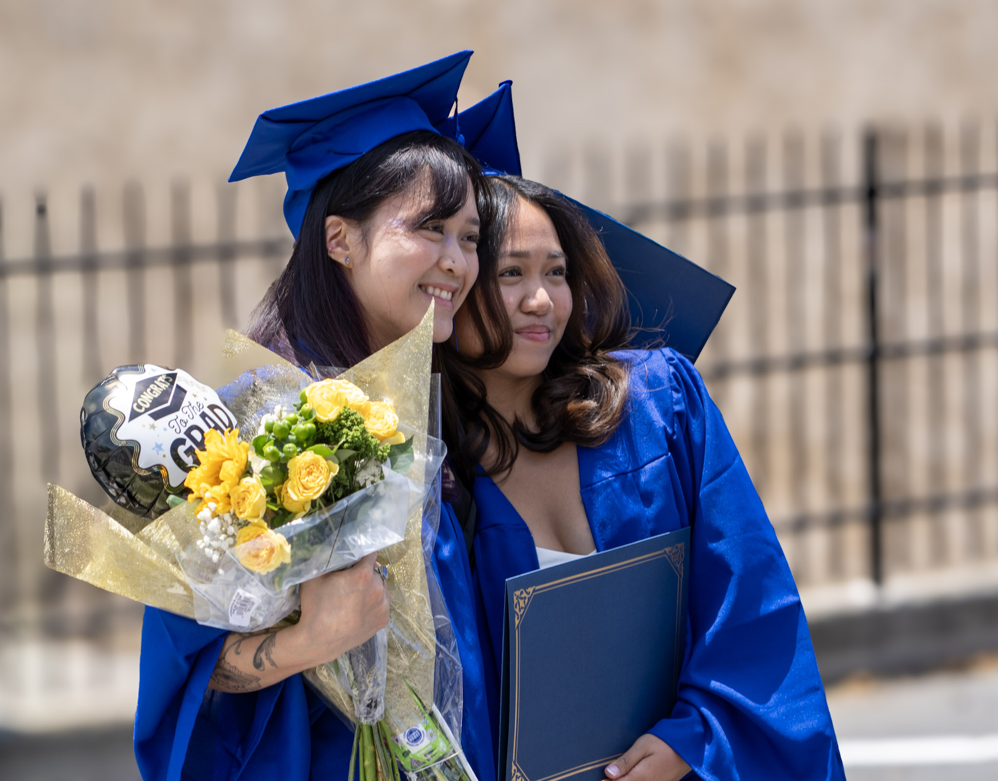 Two graduates in cap and gown with a congratulations bouquet